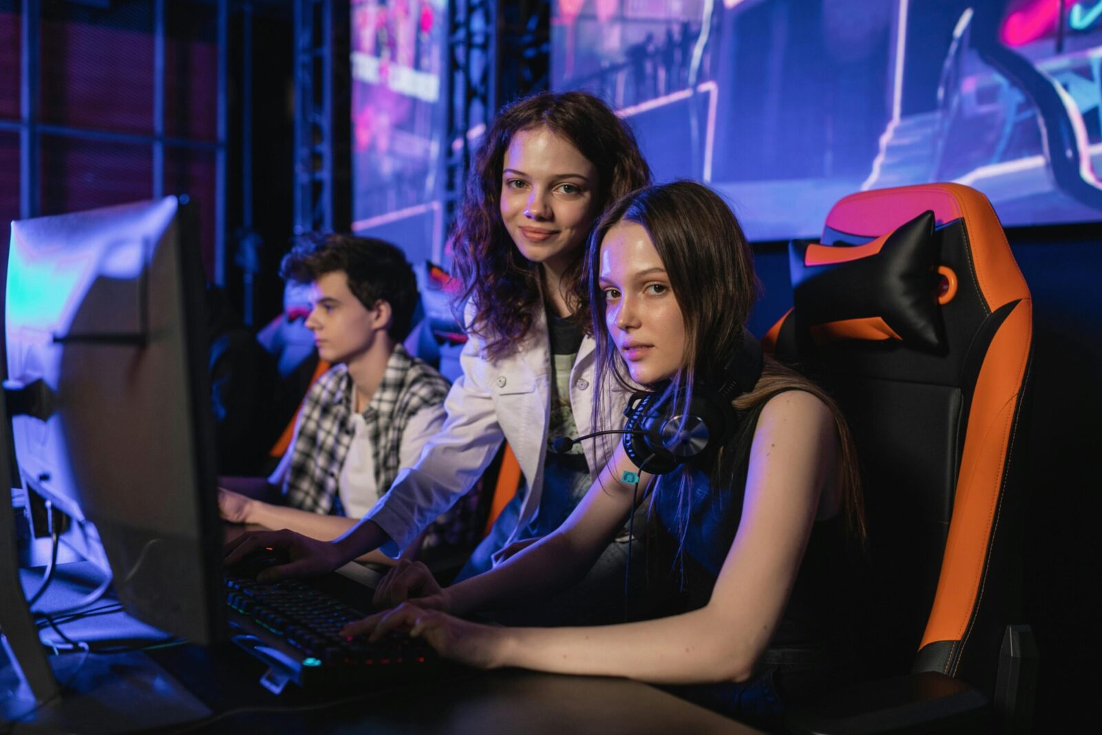 Three teenagers gaming intensely at an esports arena with computers and gaming chairs.